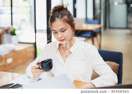 Portrait of a beautiful young woman working on a computer, documenting budget and drinking coffee during a review of the company's investment and earnings financial statements on her desk 95456563