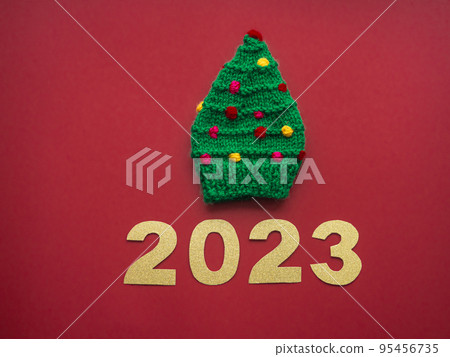 2023 and green knitted hat in the form of a Christmas tree on a red background 2023 and green knitted hat in the form of a Christmas tree on a red background 95456735