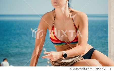 Woman in rainbow bikini. Happy tanned well looking middle aged woman in rainbow swimsuit at seaside, blue sea water in background. Holiday, vacation and recreational concept. Woman in rainbow bikini. Happy tanned well looking middle aged woman in rainbow swimsuit at seaside, blue sea water in background. Holiday, vacation and recreational concept. 95457294