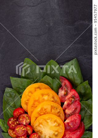 Sliced fresh tomato and basil leaf at black slate background table. Salad ingredients on tabletop Sliced fresh tomato and basil leaf at black slate background table. Salad ingredients on tabletop 95457977