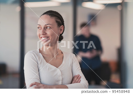 Portrait of young smiling business woman in creative open space coworking startup office. Successful businesswoman standing in office with copyspace. Coworkers working in background. 95458948