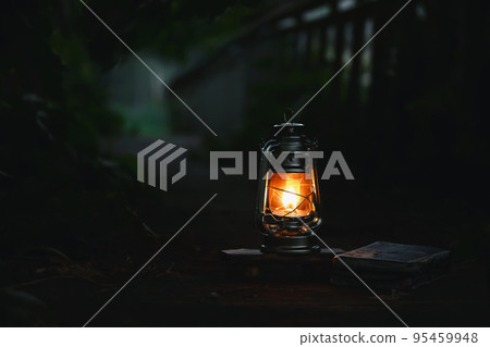 A burning light, a red lamp and a book brightly illuminate a dark night forest road A burning light, a red lamp and a book brightly illuminate a dark night forest road 95459948