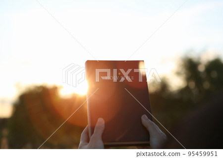 A Christian praying with the bright sunlight and the setting sun and the holy bible in both hands 95459951