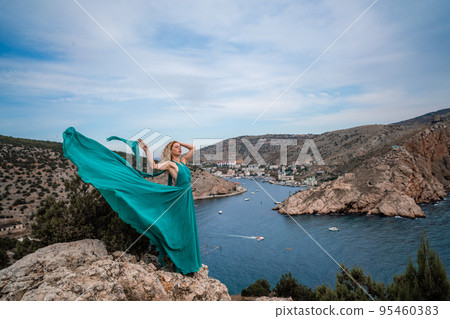 A woman in an emerald dress, a fashion model with long silk wings in a flowing dress, flying fabric on the embankment. A woman in an emerald dress, a fashion model with long silk wings in a flowing dress, flying fabric on the embankment. 95460383