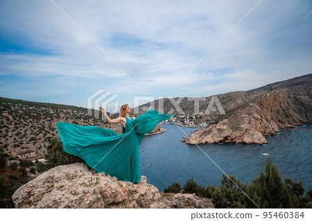 A woman in an emerald dress, a fashion model with long silk wings in a flowing dress, flying fabric on the embankment. A woman in an emerald dress, a fashion model with long silk wings in a flowing dress, flying fabric on the embankment. 95460384