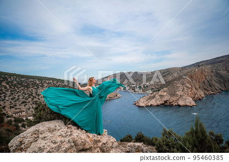 A woman in an emerald dress, a fashion model with long silk wings in a flowing dress, flying fabric on the embankment. A woman in an emerald dress, a fashion model with long silk wings in a flowing dress, flying fabric on the embankment. 95460385