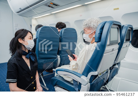A flight attendant wearing a mask and providing in-flight service 95461237