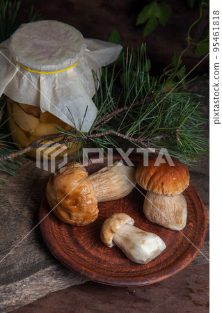 Clay plate with three porcini mushrooms commonly known as Boletus Edulis and glass jar with canned mushrooms on vintage wooden background.. Clay plate with three porcini mushrooms commonly known as Boletus Edulis and glass jar with canned mushrooms on vintage wooden background.. 95461818