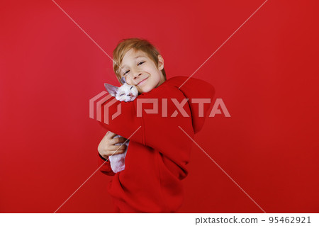 A cheerful boy in a red tracksuit hugs a little kitten and cuddles him 95462921