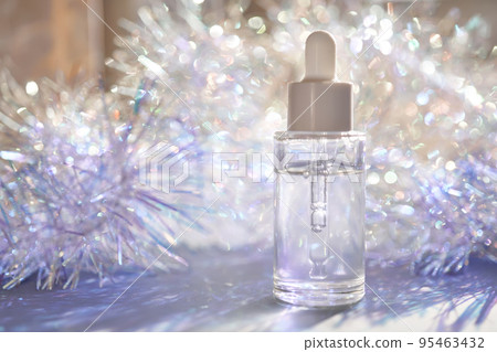 A bottle of serum with a pipette in tinsel in a Christmas theme in purple shades. A bottle of serum with a pipette in tinsel in a Christmas theme in purple shades. 95463432