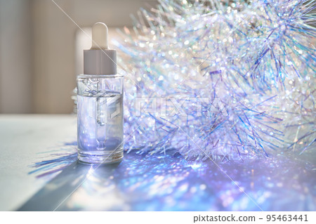 A bottle of serum with a pipette in tinsel in a Christmas theme in purple shades. A bottle of serum with a pipette in tinsel in a Christmas theme in purple shades. 95463441