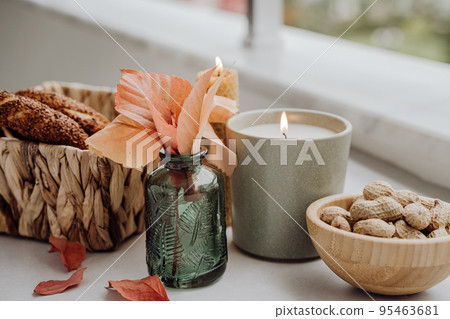 Still life candle flame, peanut, fallen leaves, wicker basket, bagel on a table, home decor in a cozy house. Autumn weekend concept. 95463681