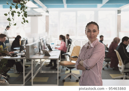 Portrait of young smiling business woman in creative open space coworking startup office. Successful businesswoman in modern office. Team of Coworkers working in background. 95463860