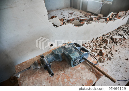 Wooden desk with electric hammer drill for construction and demolition works. Professional tool for demolishing and home renovation in room with destroyed wall. 95464129