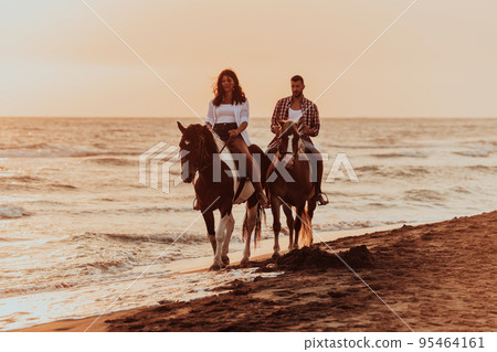 A loving couple in summer clothes riding a horse on a sandy beach at sunset. Sea and sunset in the background. Selective focus A loving couple in summer clothes riding a horse on a sandy beach at sunset. Sea and sunset in the background. Selective focus 95464161