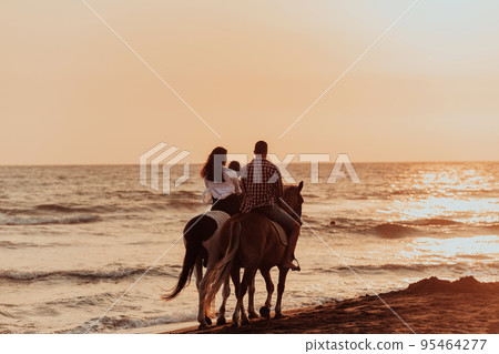 The family spends time with their children while riding horses together on a sandy beach. Selective focus  95464277