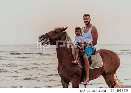 Father and son enjoy riding horses together by the sea. Selective focus Father and son enjoy riding horses together by the sea. Selective focus 95464289