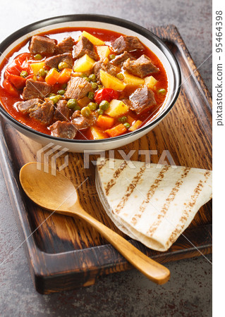 Orman Kebabi is a juicy meat dish that has plenty of peas and sliced potatoes closeup in the bowl. Vertical 95464398