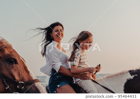 Mother and daughter enjoy riding horses together by the sea. Selective focus Mother and daughter enjoy riding horses together by the sea. Selective focus 95464431