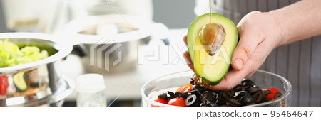 Male cook holding bottle with olive oil, watering avocado with bone, cooking healthy salad 95464647