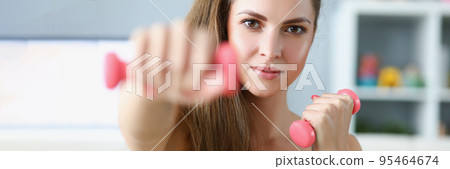 Pretty young woman performing exercise with dumbbells at home Pretty young woman performing exercise with dumbbells at home 95464674