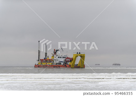 Vessel engaged in dredging at sunset time. Hopper dredger working at sea. Ship excavating material from a water environment. Vessel engaged in dredging at sunset time. Hopper dredger working at sea. Ship excavating material from a water environment. 95466355