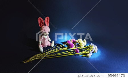 A bouquet of flowers and a rabbit stuffed animal illuminated by a spotlight in a dark place A bouquet of flowers and a rabbit stuffed animal illuminated by a spotlight in a dark place 95466473