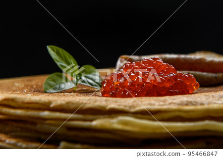 Stack of pancakes with red caviar on black background, close up 95466847