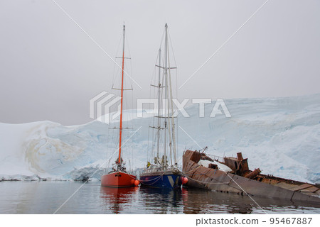 Two sailing yachts in the antarctic sea moored to rusty wreck Two sailing yachts in the antarctic sea moored to rusty wreck 95467887