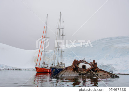Two sailing yachts in the antarctic sea moored to rusty wreck Two sailing yachts in the antarctic sea moored to rusty wreck 95467888