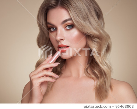 A beautiful young blonde woman applying lipstick 95468008