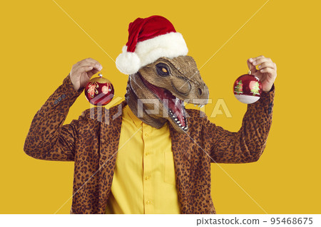 Funny man in dinosaur mask, Christmas hat and leopard suit holding Xmas tree balls 95468675