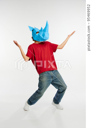 Dance. Young man in red t-shirt with cardboard animal mask on his head isolated on white background. Concept of art, fashion, theater, funny meme emotions. 95469952