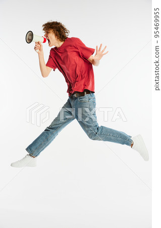 Full length portrait of excited young man jumping and shouting at megaphone isolated over white background. Sport, dance, fitness, happiness 95469955