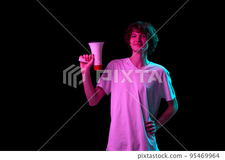 Composed young man standing with megaphone isolated over dark background in neon. Concept of sport, betting, sales, news 95469964