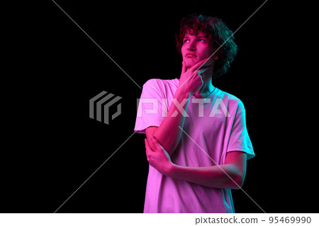 Thinking, dreaming. Half-length portrait of young man with smart facial expression isolated over dark background in purple neon light. Emotions, youth, sales, ad Thinking, dreaming. Half-length portrait of young man with smart facial expression isolated over dark background in purple neon light. Emotions, youth, sales, ad 95469990