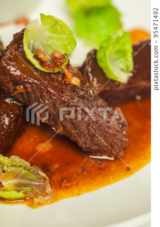 Delicious veal cheeks in red sauce closeup on a white plate on white background Delicious veal cheeks in red sauce closeup on a white plate on white background 95471492