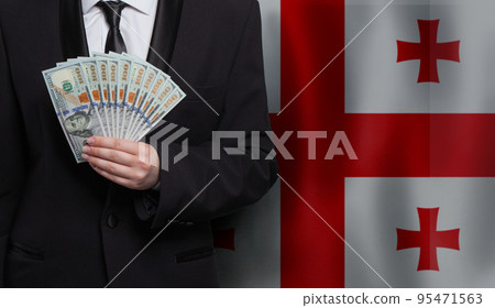 Georgian business man hand showing US 100 dollar bills against flag of Georgia background Georgian business man hand showing US 100 dollar bills against flag of Georgia background 95471563