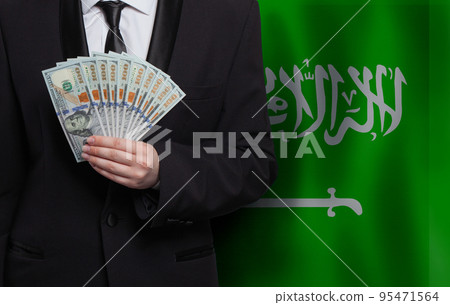 100 US dollar bills money banknotes in hand against flag of Saudi Arabia background 100 US dollar bills money banknotes in hand against flag of Saudi Arabia background 95471564
