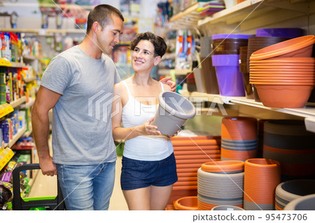 Happy married couple choosing and buying flower pots in the horticultural section of supermarket Happy married couple choosing and buying flower pots in the horticultural section of supermarket 95473706