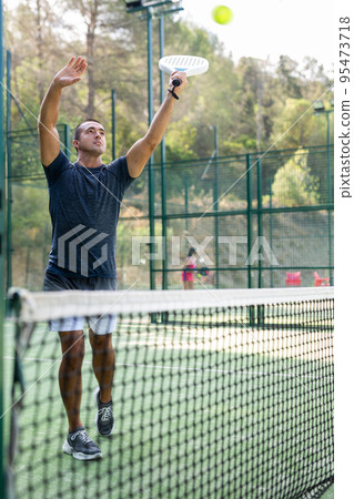 Athletic man plays padel. View through tennis net outdoor Athletic man plays padel. View through tennis net outdoor 95473718