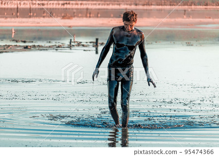 Man applying black healing clay. Mud spa on the shore of salt lake. Swimming in the nutrient-rich mud of the mud lake near the Sea of Azov, Crimea, mud lake Chokrak. Russia Man applying black healing clay. Mud spa on the shore of salt lake. Swimming in the nutrient-rich mud of the mud lake near the Sea of Azov, Crimea, mud lake Chokrak. Russia 95474366