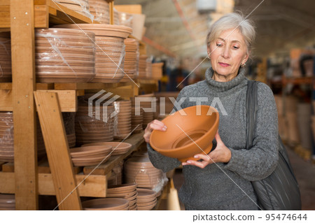 Eldrely woman selecting earthenware crockery in shop 95474644