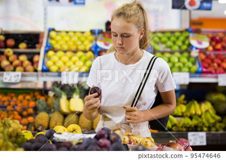 Focused fifteen-year-old girl chooses plums on the counter 95474646