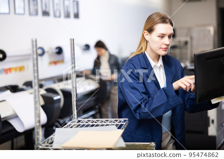 Female employee of the printing house adjusts the plotter using computer Female employee of the printing house adjusts the plotter using computer 95474862