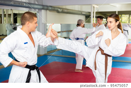 Young girl in white kimono practicing kicking with male opponent 95475057