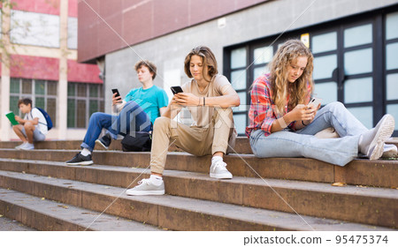 Teenage friends boy and girl holding phones and browsing Teenage friends boy and girl holding phones and browsing 95475374