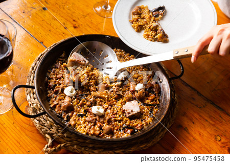 Client serving paella montana with mushrooms and pork trotters into plate Client serving paella montana with mushrooms and pork trotters into plate 95475458