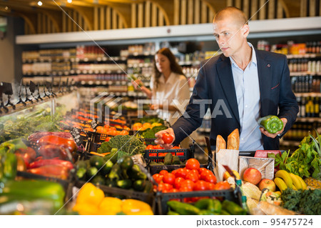 Young confident man selects fresh vegetables in the supermarket 95475724