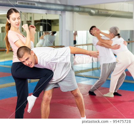 Girl practicing elbow and knee strikes with arm hold to male sparring partner at gym 95475728